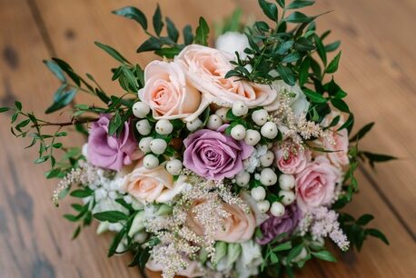 A bouquet of pink and purple roses, white berries, and greenery rests on a wooden floor.